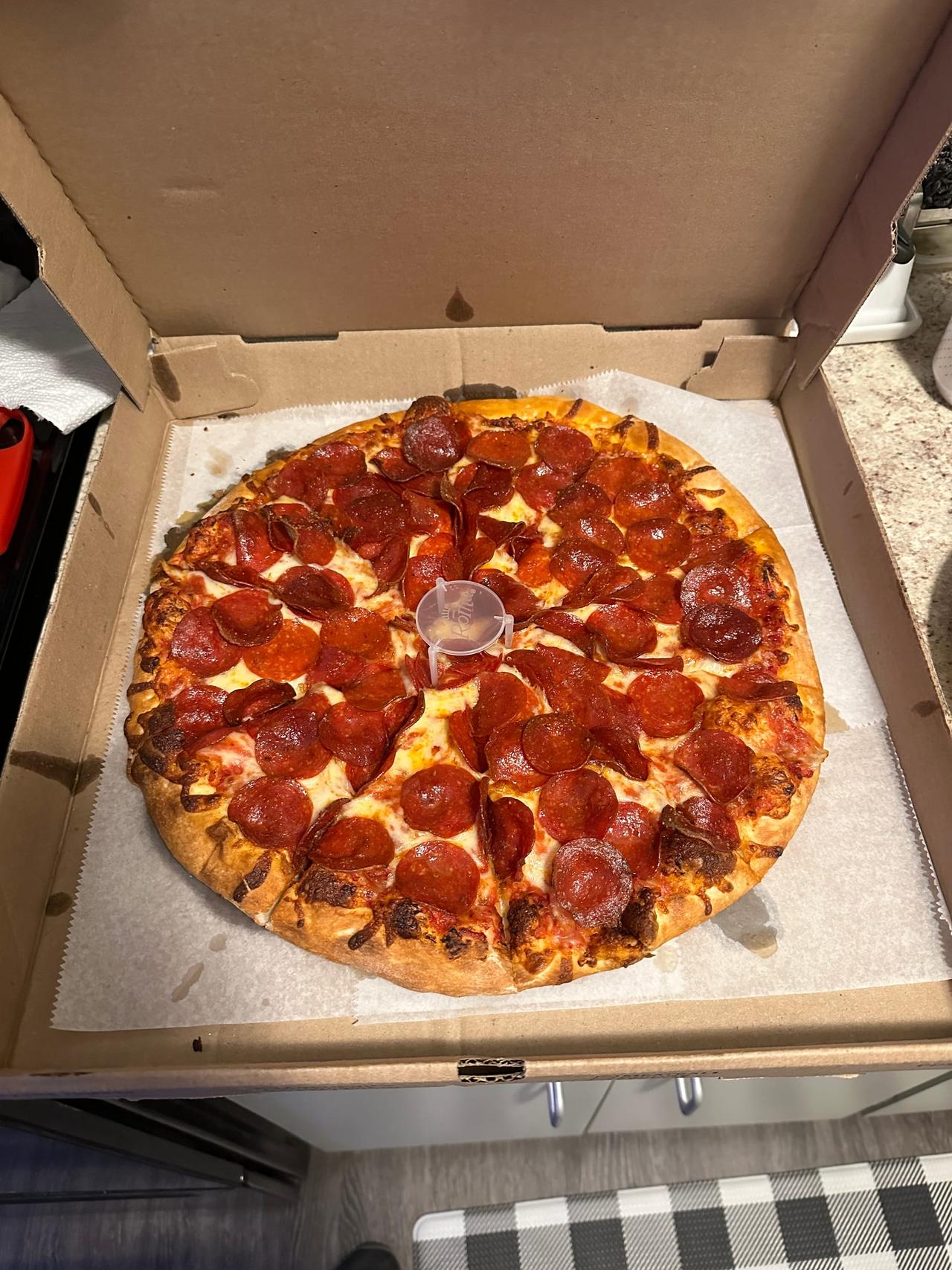 Pepperoni pizza covered edge to edge in crisp, cupped pepperoni with a golden, blistered crust, sitting in a plain cardboard box.